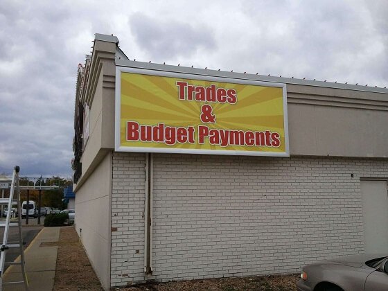 Large outdoor banner mounted on a building exterior displaying promotional messaging. Used for storefront advertising, business signage, and long-term outdoor visibility.